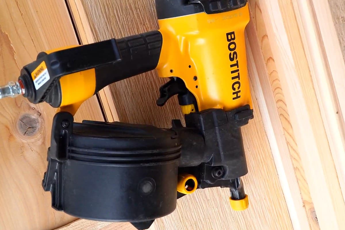 Bostitch coil nailer resting on stacked cedar rails during an Ovora cedar fence build