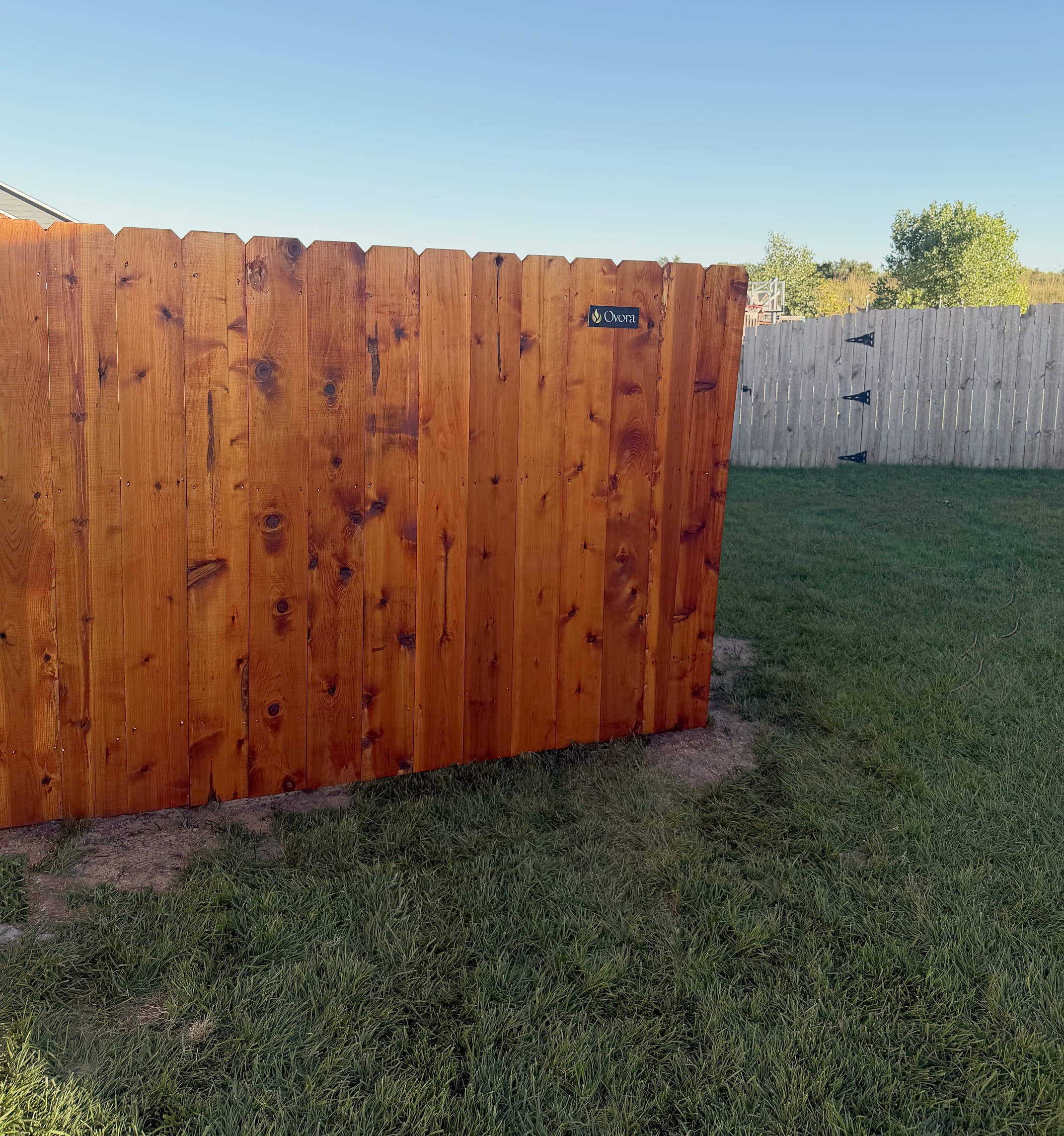 Cedar privacy fence in a red-toned stain with an Ovora plate mounted on it in Maize, Kansas