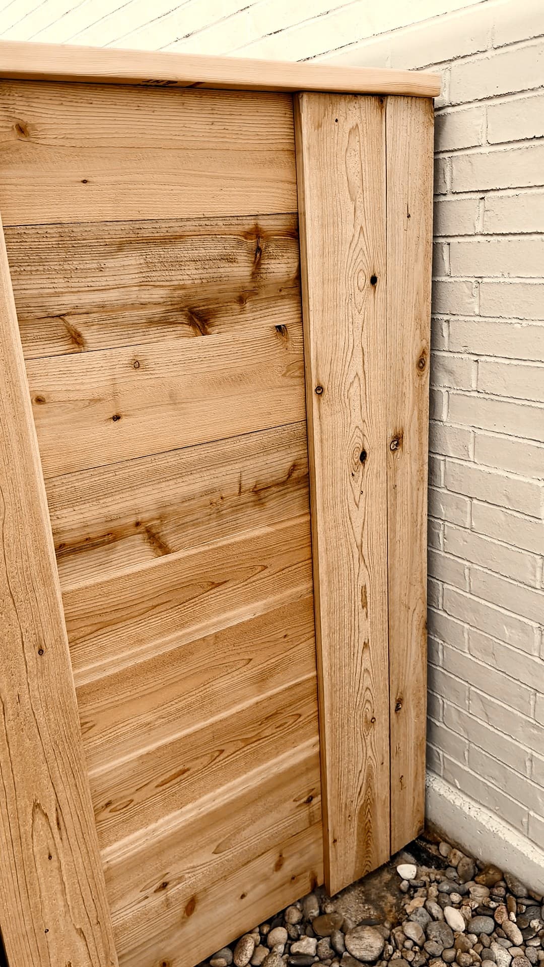 Corner of a horizontal cedar fence with a flat cedar cap against a brick wall in Andale, Kansas