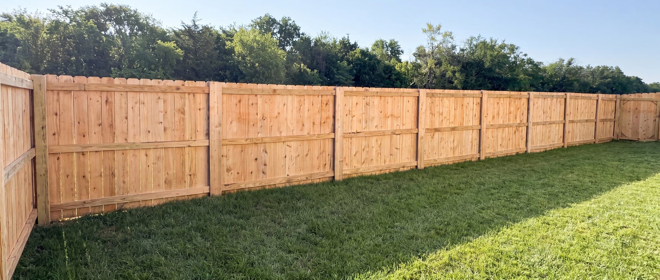 Cedar privacy fence run with a gate at the far end of a backyard in the Wichita metro