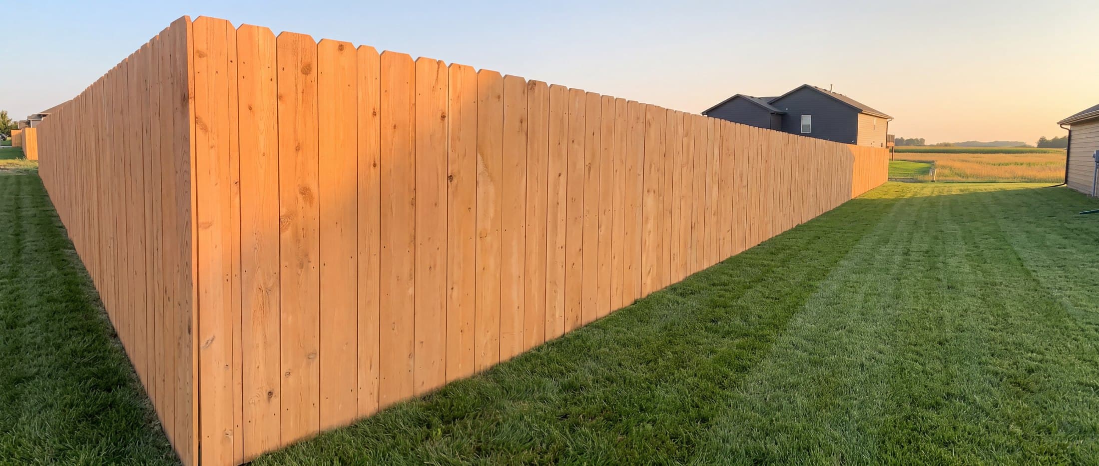 Cedar privacy fence line receding toward open Kansas farmland at dusk in Andover