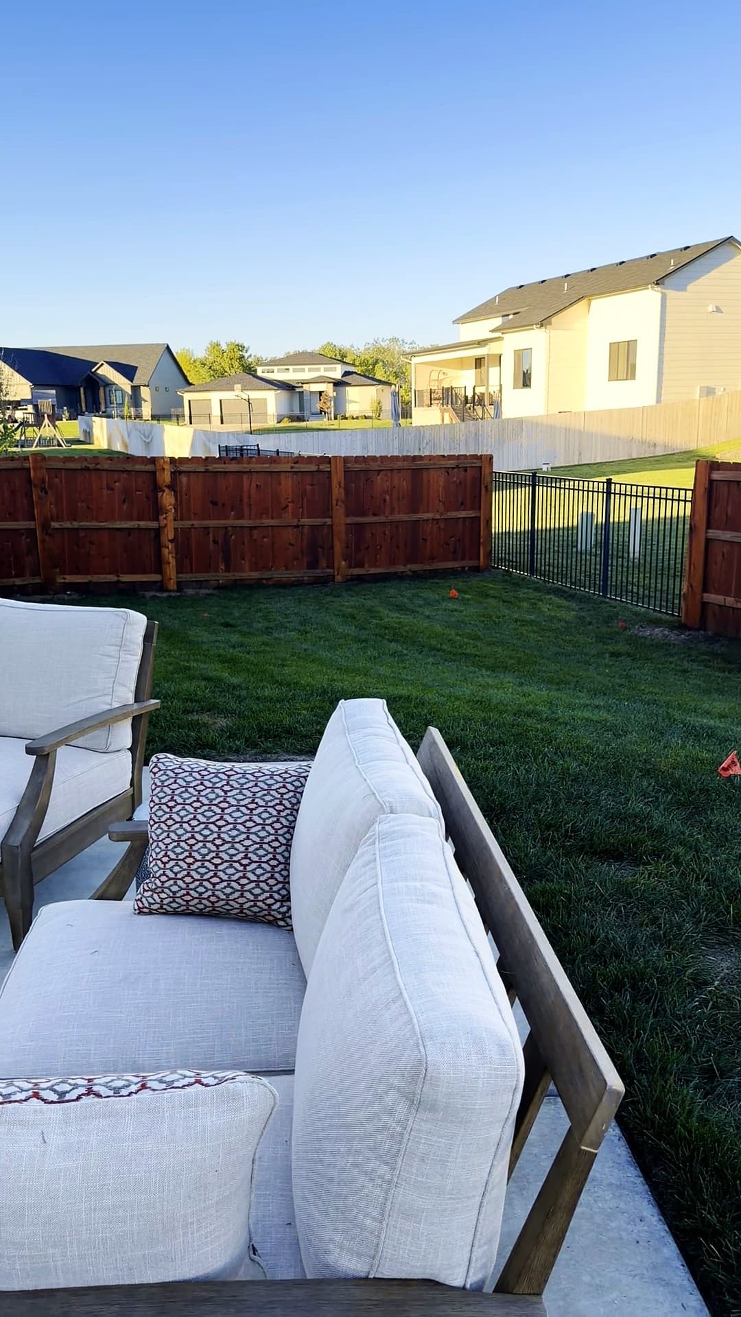Stained cedar privacy fence and a black iron fence section seen from a backyard patio in Maize, Kansas
