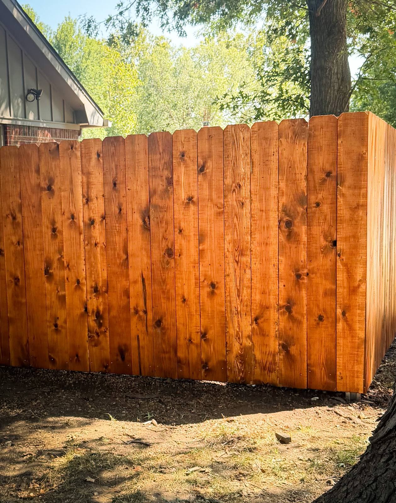 Corner section of a stained cedar privacy fence in golden light beside a house in Derby, Kansas