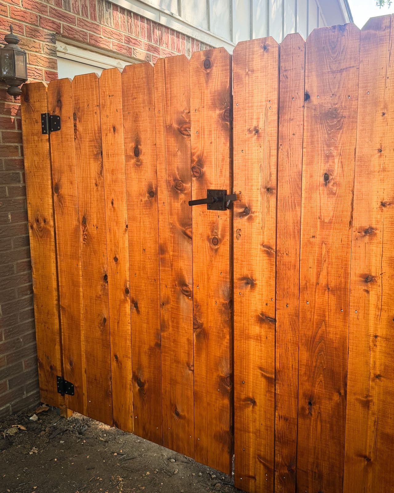 Stained cedar gate with black latch and hinges against a red brick wall in Derby, Kansas