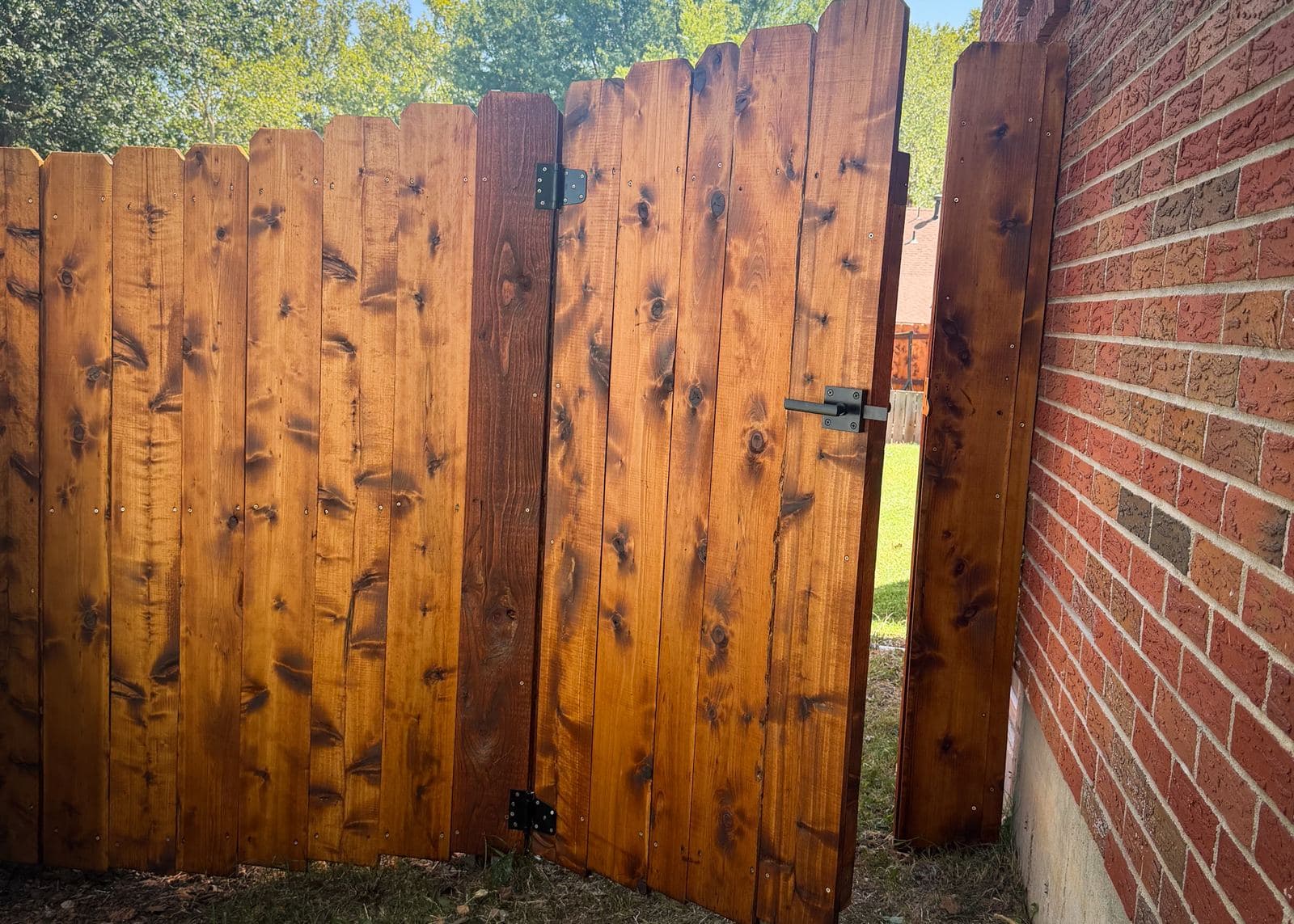 An open cedar privacy fence gate with black hinges in a Wichita-area backyard