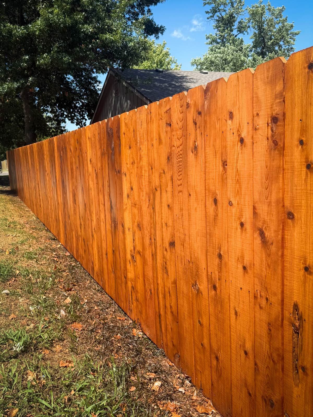 Stained cedar privacy fence running the length of a backyard under a blue sky in Derby, Kansas