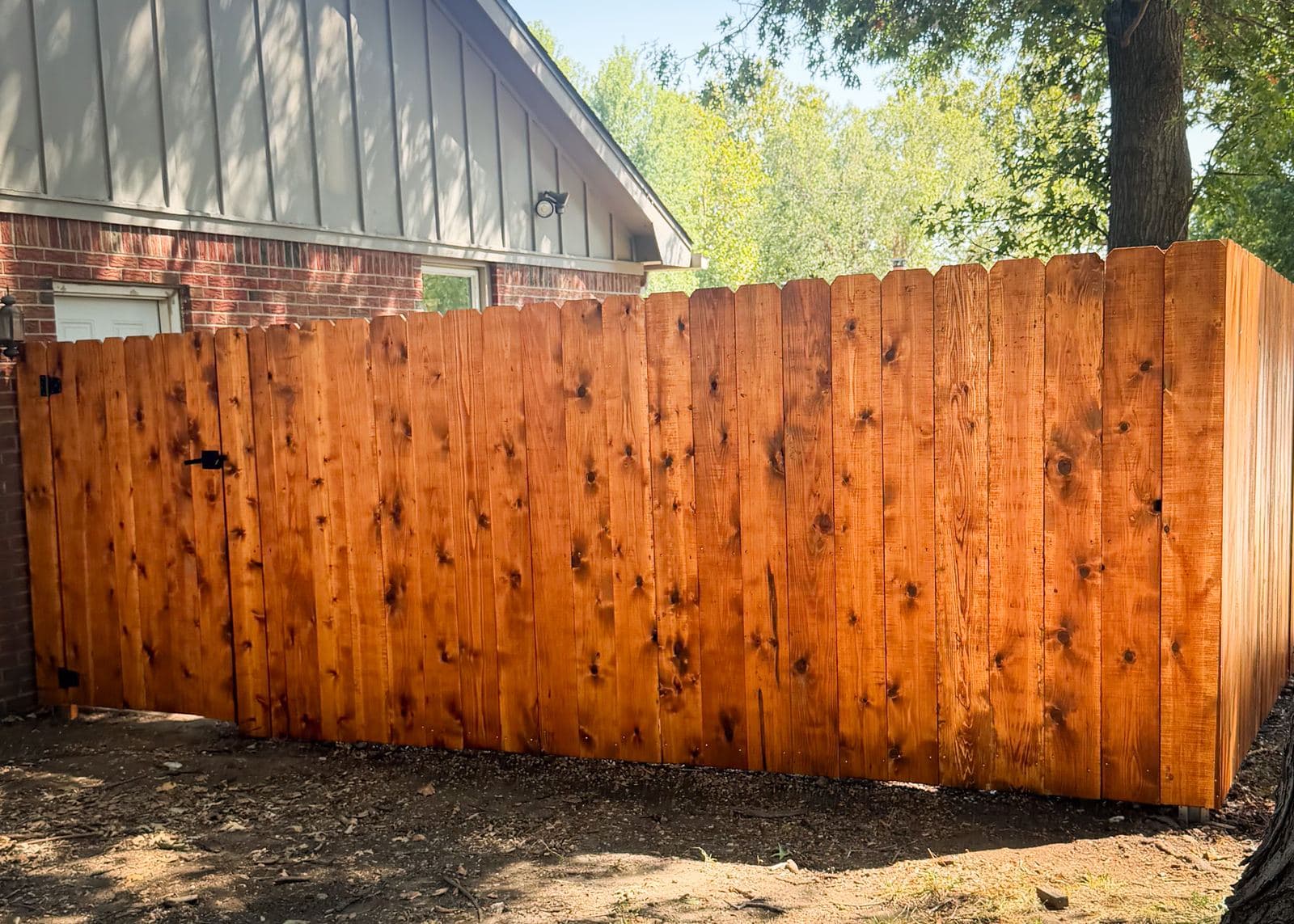 Stained cedar privacy fence with a walk gate beside a brick house in Derby, Kansas